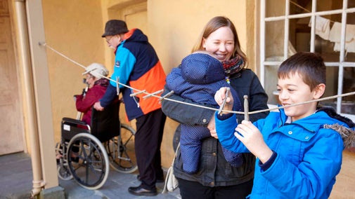 Ymwelydd ifanc yn chwarae gyda phegiau yn yr iard yn Llanerchaeron tra bod un arall yn ei wylio